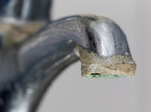 Close-up of a curved, corroded metal pipe with a crusty, green-edged open end.